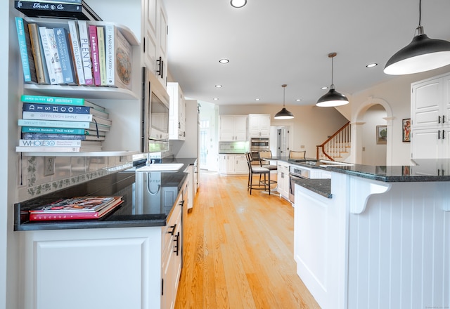 kitchen with stainless steel appliances, backsplash, pendant lighting, light hardwood / wood-style floors, and white cabinets