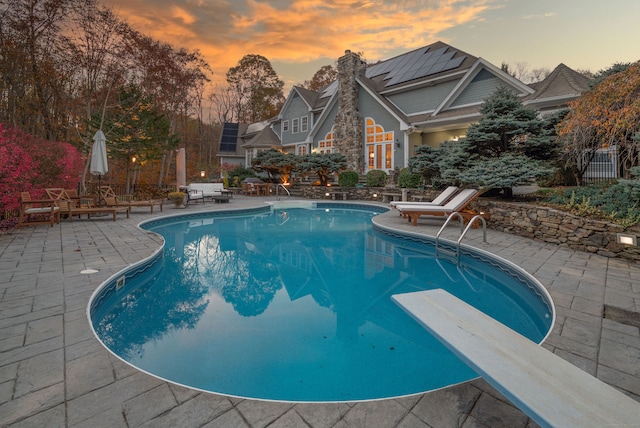 pool at dusk with a diving board and a patio area