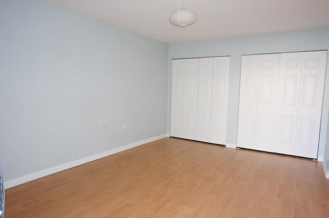 unfurnished bedroom featuring wood-type flooring and two closets