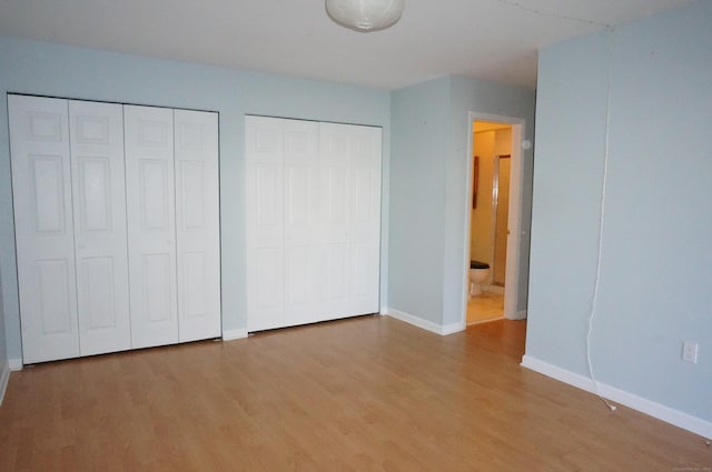 unfurnished bedroom featuring wood-type flooring and multiple closets