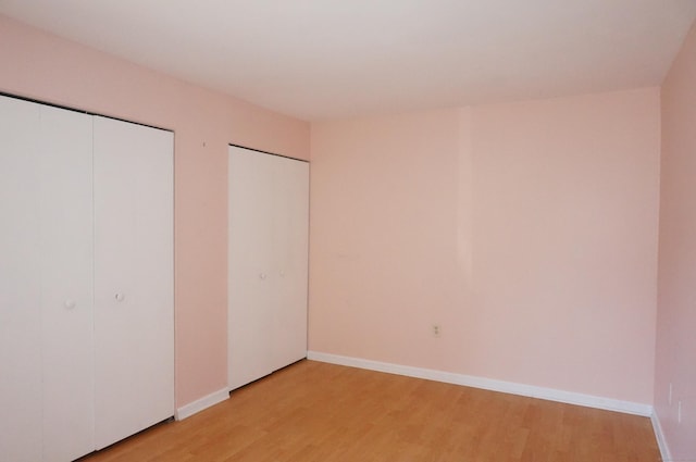 unfurnished bedroom featuring multiple closets and light hardwood / wood-style flooring