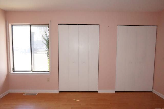 unfurnished bedroom featuring multiple closets, light hardwood / wood-style flooring, and multiple windows