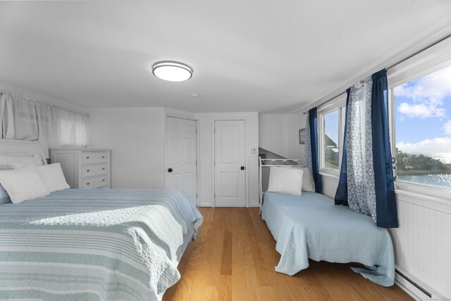 bedroom featuring light wood-type flooring, multiple windows, and a baseboard heating unit