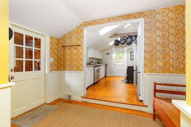 kitchen featuring white cabinets, stainless steel range, light wood-type flooring, and lofted ceiling with skylight