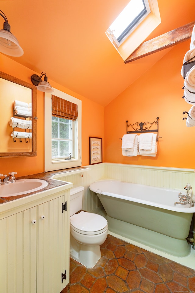 bathroom with lofted ceiling with skylight, a tub to relax in, vanity, tile patterned floors, and toilet