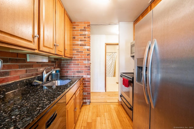 kitchen featuring sink, dark stone countertops, tasteful backsplash, light hardwood / wood-style floors, and stainless steel appliances