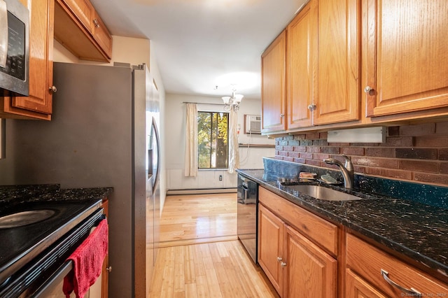 kitchen featuring appliances with stainless steel finishes, sink, an inviting chandelier, light hardwood / wood-style flooring, and dark stone countertops