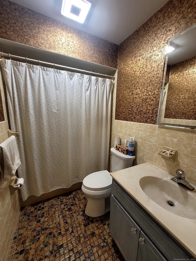 bathroom featuring toilet, vanity, and tile walls