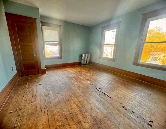 empty room featuring plenty of natural light, wood-type flooring, and radiator