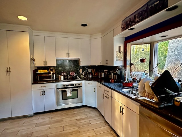 kitchen with light wood-type flooring, tasteful backsplash, ventilation hood, stainless steel appliances, and white cabinetry