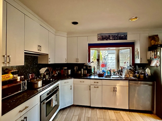 kitchen featuring white cabinetry, sink, light hardwood / wood-style flooring, backsplash, and appliances with stainless steel finishes