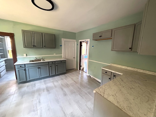 kitchen with light wood-type flooring, sink, light stone counters, and gray cabinetry