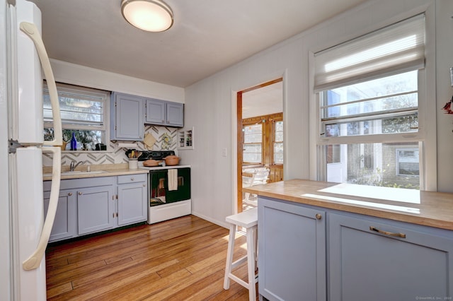 kitchen with sink, backsplash, light hardwood / wood-style floors, white appliances, and gray cabinets