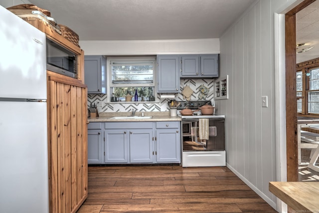 kitchen with sink, dark wood-type flooring, backsplash, white appliances, and wooden walls