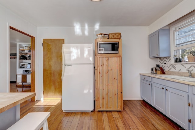 kitchen featuring white refrigerator, stainless steel microwave, light wood-type flooring, and sink