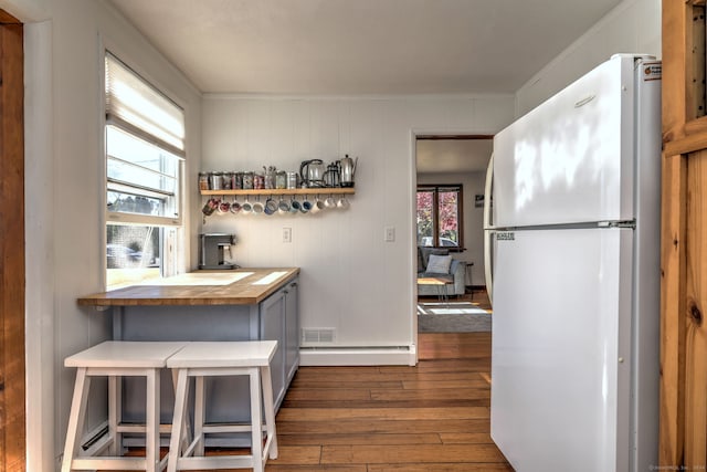 kitchen with a kitchen breakfast bar, a baseboard heating unit, dark wood-type flooring, white refrigerator, and butcher block countertops