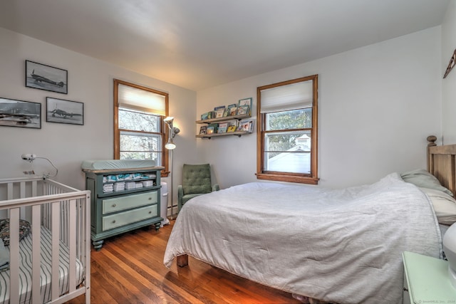 bedroom with hardwood / wood-style floors, a baseboard radiator, and multiple windows