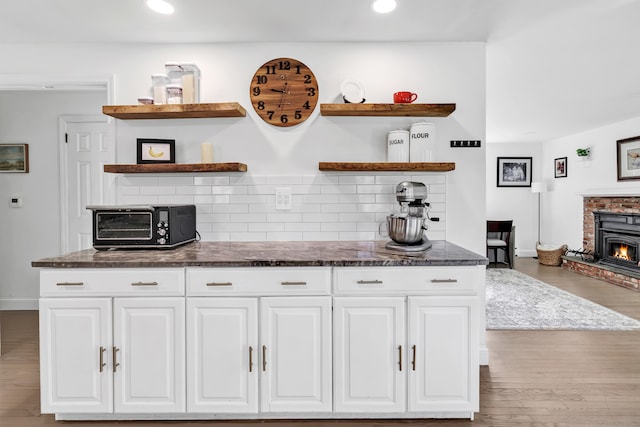 kitchen with decorative backsplash, light hardwood / wood-style flooring, dark stone countertops, white cabinets, and a wood stove