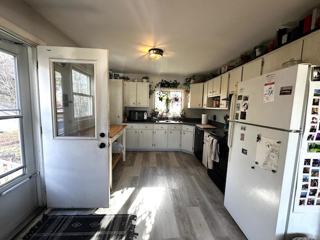 kitchen with black appliances, a healthy amount of sunlight, cream cabinetry, and hardwood / wood-style flooring