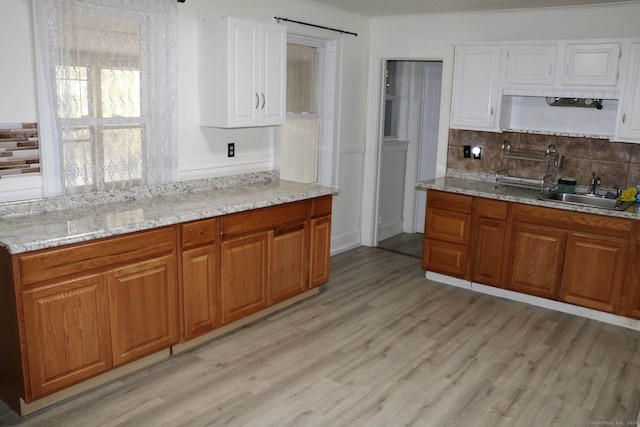 kitchen with decorative backsplash, light hardwood / wood-style floors, sink, and light stone counters