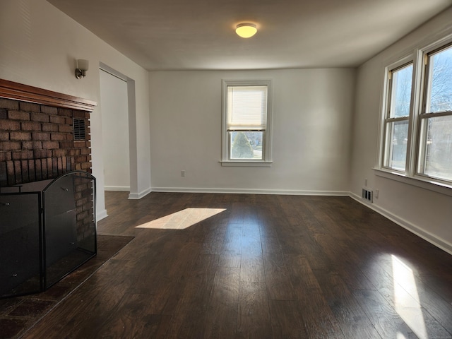 unfurnished living room with a brick fireplace, plenty of natural light, and dark wood-type flooring