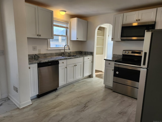 kitchen featuring sink, white cabinetry, stainless steel appliances, and dark stone counters