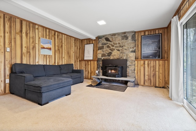 carpeted living room featuring wooden walls, a stone fireplace, and beam ceiling