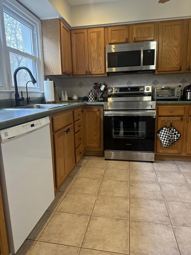 kitchen featuring stainless steel appliances, sink, light tile patterned floors, and backsplash