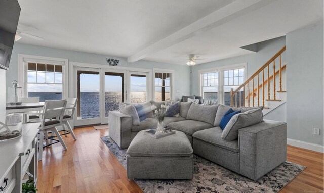 living room with a water view, ceiling fan, light wood-type flooring, and beamed ceiling