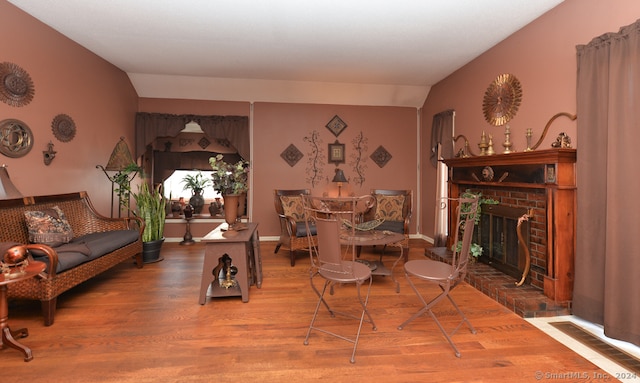 living room featuring a brick fireplace, lofted ceiling, and wood-type flooring