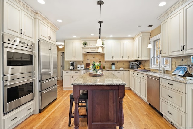 kitchen with a kitchen island, appliances with stainless steel finishes, decorative light fixtures, sink, and light hardwood / wood-style flooring