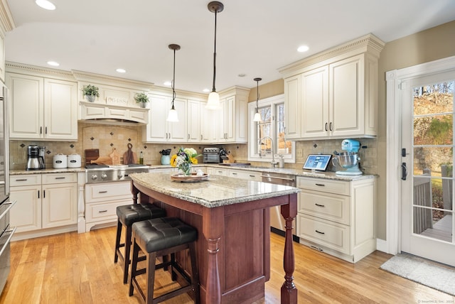 kitchen featuring stainless steel appliances, light stone counters, tasteful backsplash, light wood-type flooring, and pendant lighting