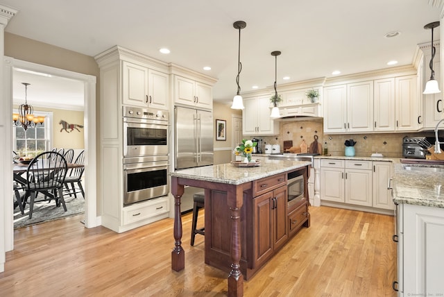 kitchen featuring a breakfast bar, pendant lighting, built in appliances, and light hardwood / wood-style flooring