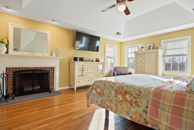 bedroom with a brick fireplace, ceiling fan, light hardwood / wood-style flooring, and vaulted ceiling