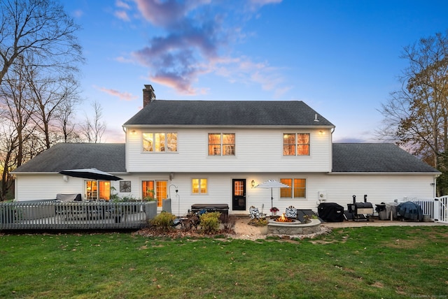 back house at dusk with a patio area, a lawn, and a wooden deck