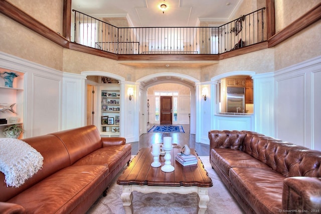 living room featuring a high ceiling, built in shelves, ornate columns, ornamental molding, and light hardwood / wood-style floors