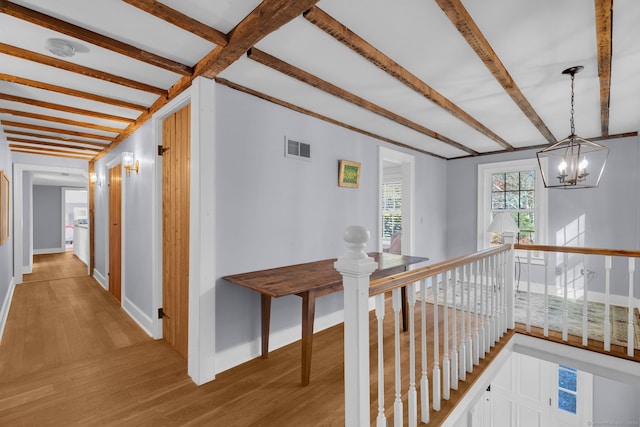 hall with hardwood / wood-style floors, beamed ceiling, and a chandelier