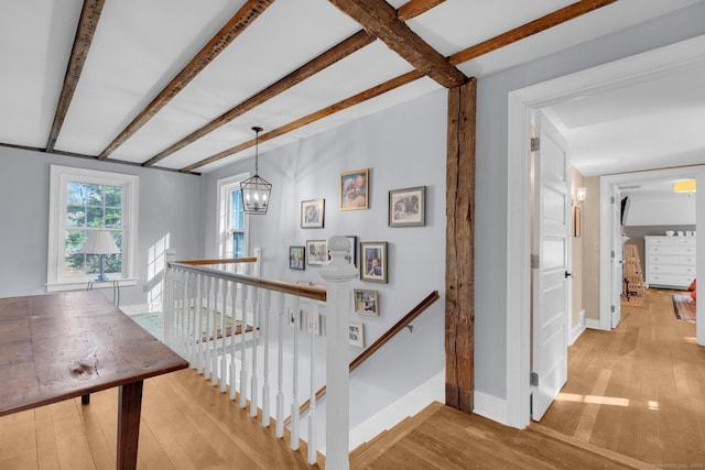 hall featuring light hardwood / wood-style floors, beam ceiling, and an inviting chandelier