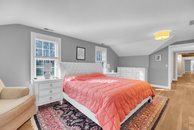 bedroom featuring multiple windows, lofted ceiling, and light hardwood / wood-style flooring