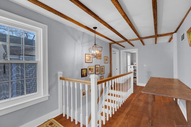 hall featuring dark wood-type flooring, beam ceiling, and an inviting chandelier