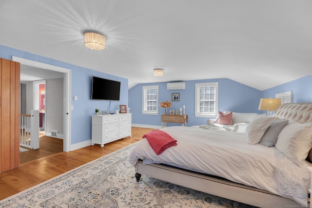 bedroom featuring light wood-type flooring, an AC wall unit, and vaulted ceiling