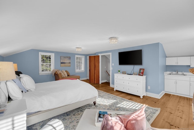 bedroom featuring sink, light wood-type flooring, and vaulted ceiling