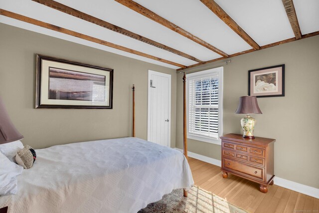 bedroom with light hardwood / wood-style floors and beam ceiling