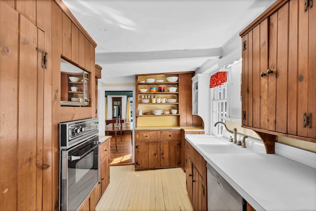 kitchen featuring sink, light hardwood / wood-style flooring, beamed ceiling, stainless steel dishwasher, and black oven