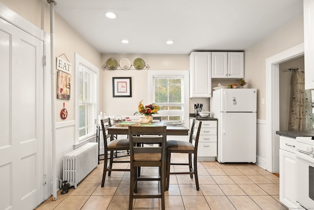 kitchen featuring white cabinets, radiator heating unit, light tile patterned floors, and white appliances