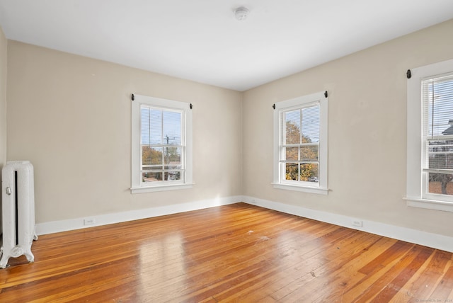 unfurnished room featuring radiator heating unit, wood-type flooring, and plenty of natural light