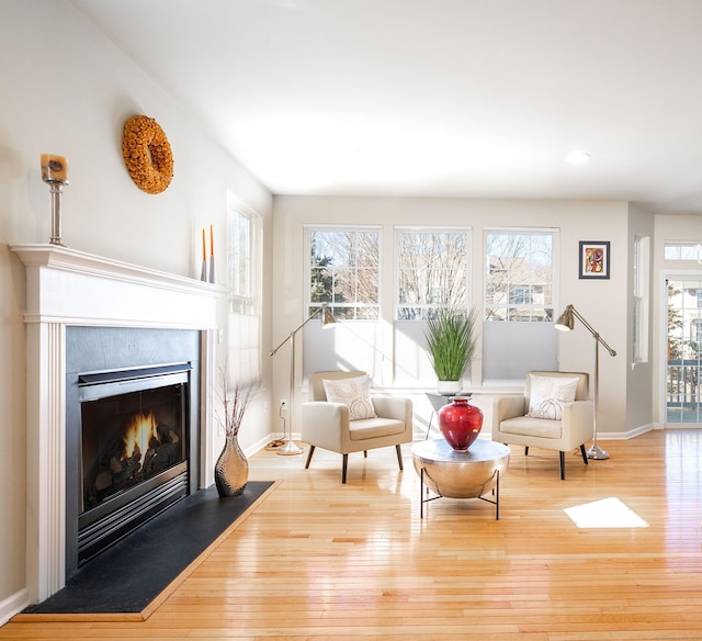 sitting room featuring a glass covered fireplace, wood finished floors, and baseboards