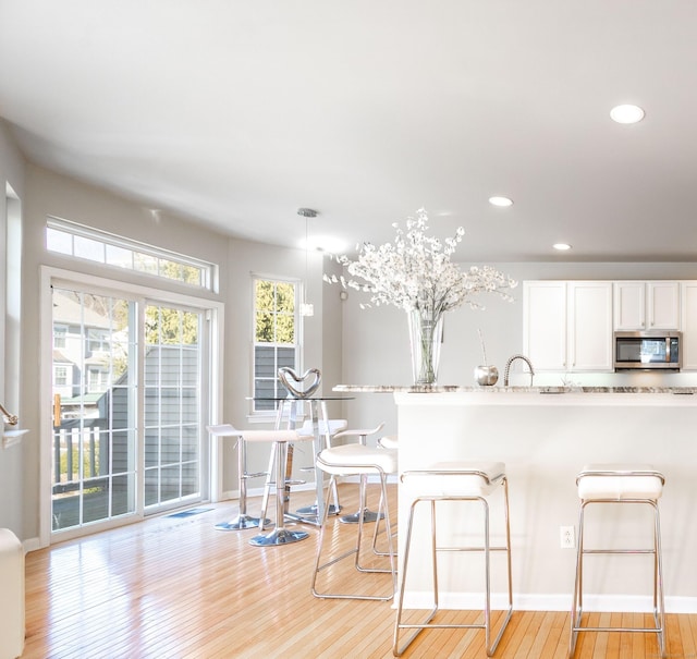 kitchen with stainless steel microwave, recessed lighting, light wood-style floors, a breakfast bar area, and white cabinets