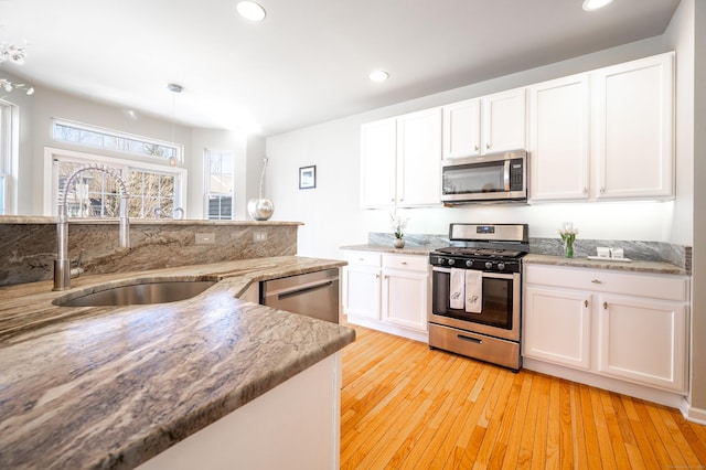 kitchen with light stone counters, light wood-style flooring, appliances with stainless steel finishes, white cabinets, and a sink