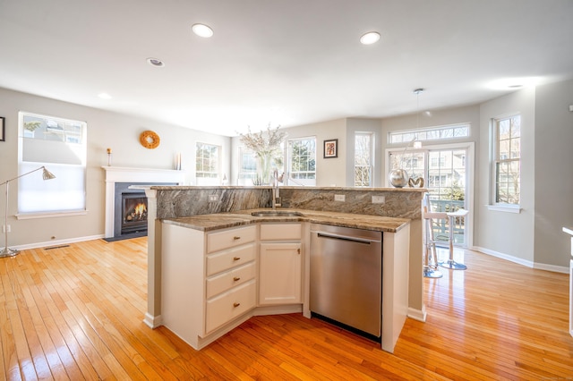 kitchen featuring light stone counters, a fireplace with flush hearth, a sink, light wood-style floors, and stainless steel dishwasher